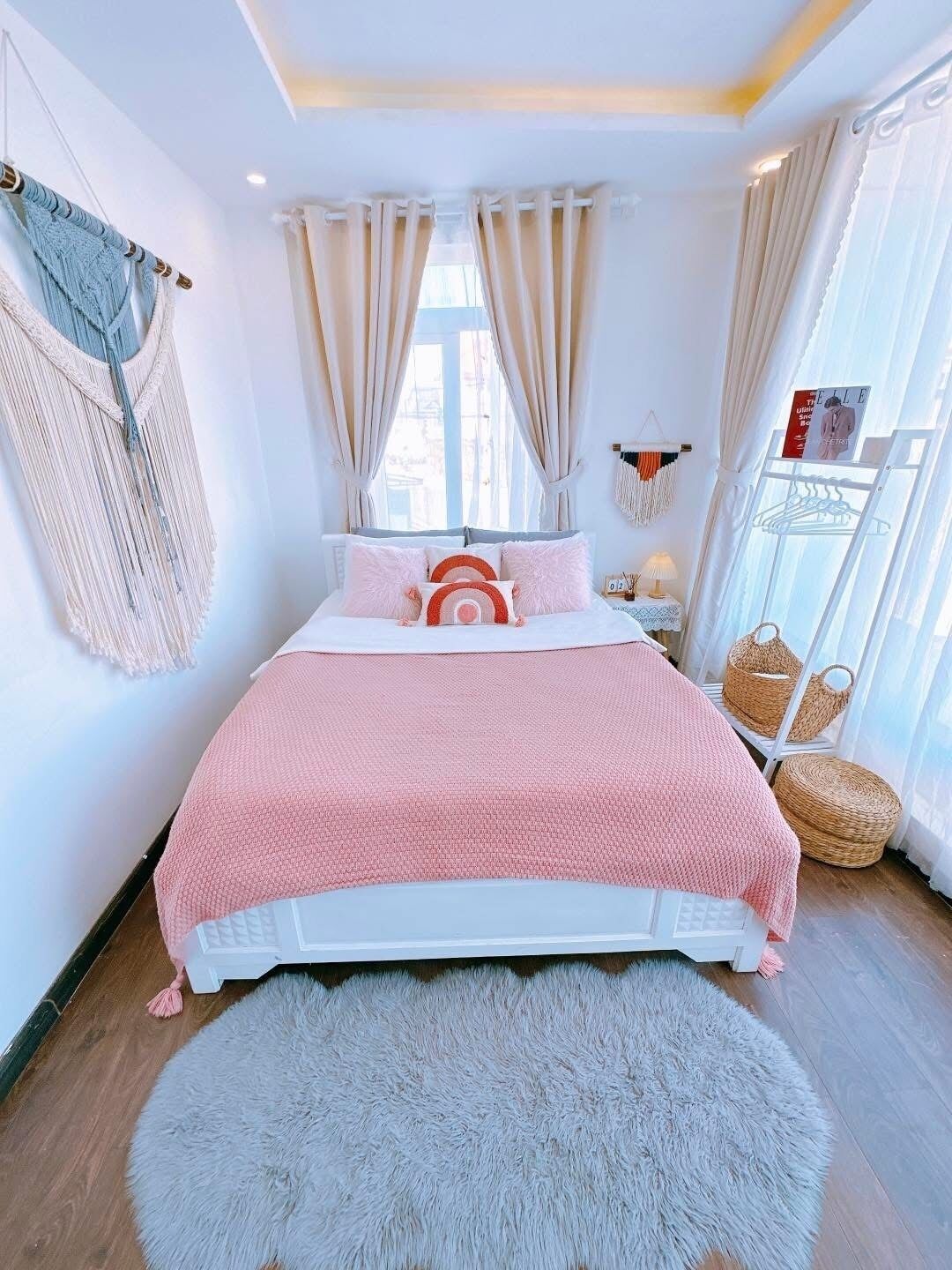 A bedroom with a bed, a large window with curtains, a wall-mounted rack with baskets, and a fluffy rug.