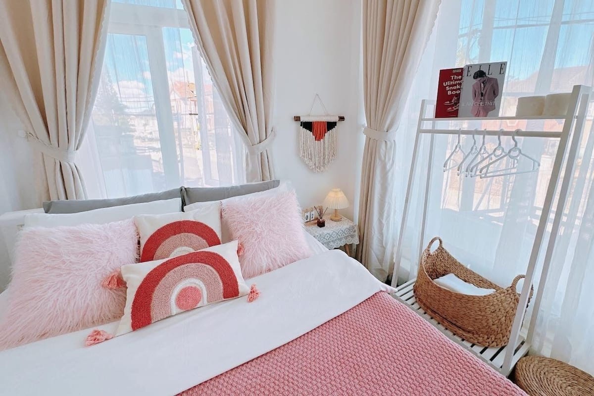 A neatly arranged bedroom with a bed, pillows, a bedside table with a lamp, and a view of the outside through large windows.