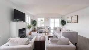 A living room with a fireplace, two sofas, a coffee table, and a TV mounted on the wall. - Luxury family retreat on lakefront with breathtaking view, game room, gym &more! (Kawartha Lakes)