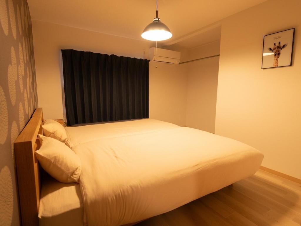 A single bed with a wooden headboard, a ceiling light, an air conditioning unit, and a framed picture on the wall.