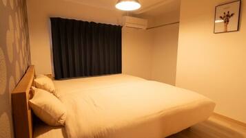 A single bed with a wooden headboard, a ceiling light, an air conditioning unit, and a framed picture on the wall.