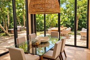 A modern dining area with a glass table, white chairs, and a woven pendant light. - Corasol Villa · 4 King Suites & Private Pool (Playa del Carmen)