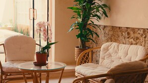 A cozy seating area with wicker chairs and a cushioned sofa, a glass table with a potted orchid, and a large potted plant against a textured wall. - THE TWO BULLS, QUADRUPLE ROOM (Mérida)
