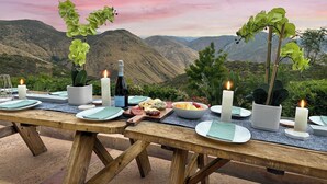 Mobiliario de comedor al aire libre con vistas panorámicas a la montaña, mesa de madera, velas y diversos alimentos.