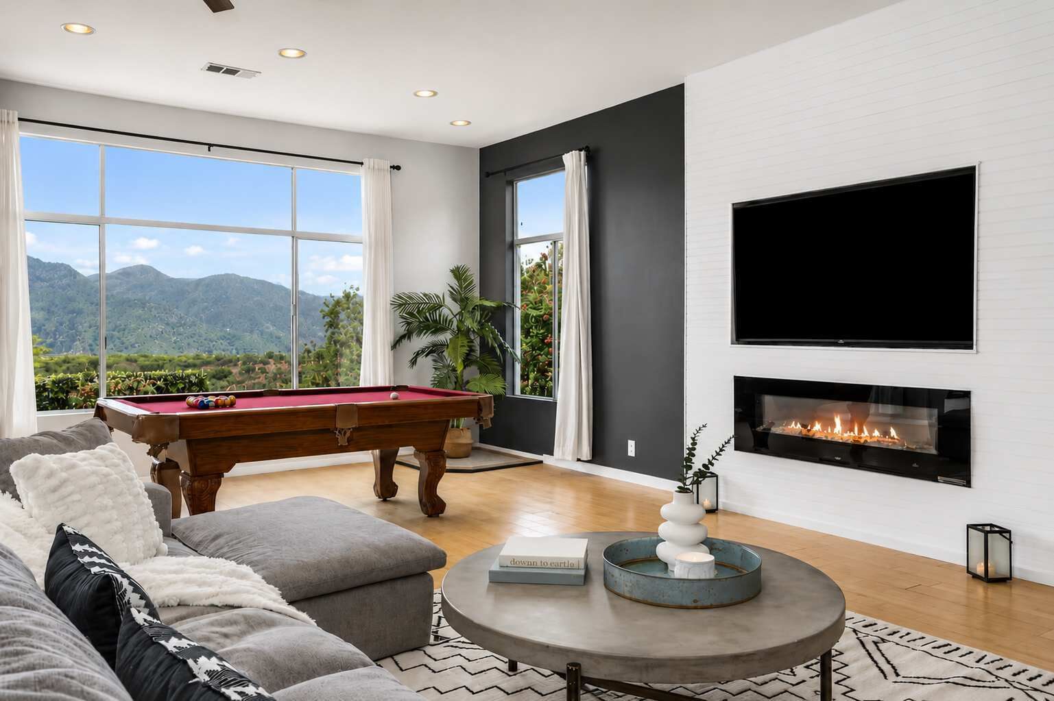 A modern living room with a pool table, comfortable seating, a fireplace, and a large TV.
