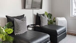 Un salon moderne avec deux canapés en cuir noir, un grand téléviseur à écran plat fixé au mur, une petite table d’appoint ronde et une grande plante en pot.