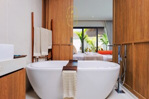 A modern bathroom with a large freestanding bathtub, wooden cabinetry, and a view of a bedroom with a bed and plants. - Elegant 3-Bedroom Private Pool Villa, Perfect for Long Stays (Tambon Rawai)