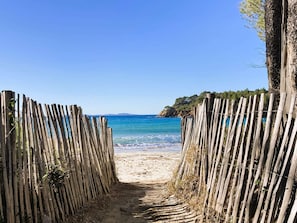 A wooden pathway leading to a beach with clear blue water and a distant view of a mountainous coastline. - Air-conditioned villa with swimming pool and sea view for 8 guests in the heart of the Valcros... (LA LONDE LES MAURES)
