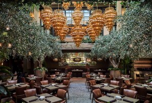 Een restaurant met meerdere tafels en stoelen, een kroonluchter en planten.