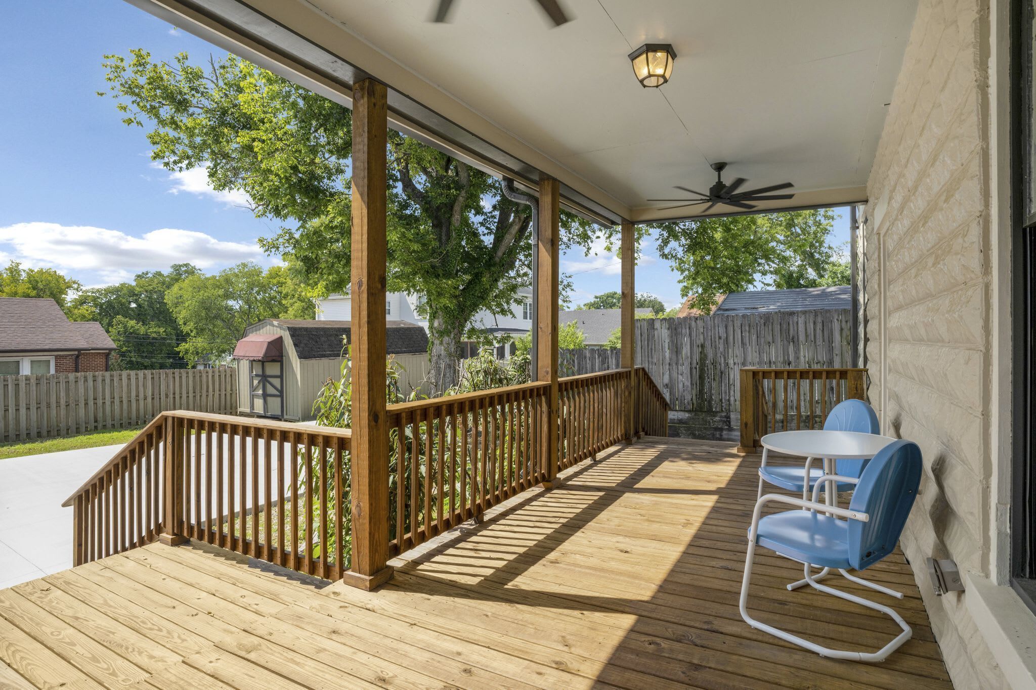 A covered outdoor deck with a wooden railing, a ceiling fan, and a table with chairs.