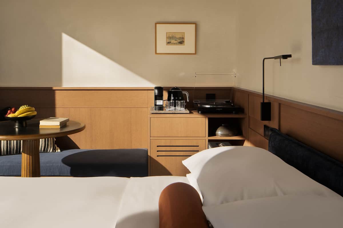 A modern hotel room with a bed, bedside table, and a desk area with a coffee maker and a lamp.