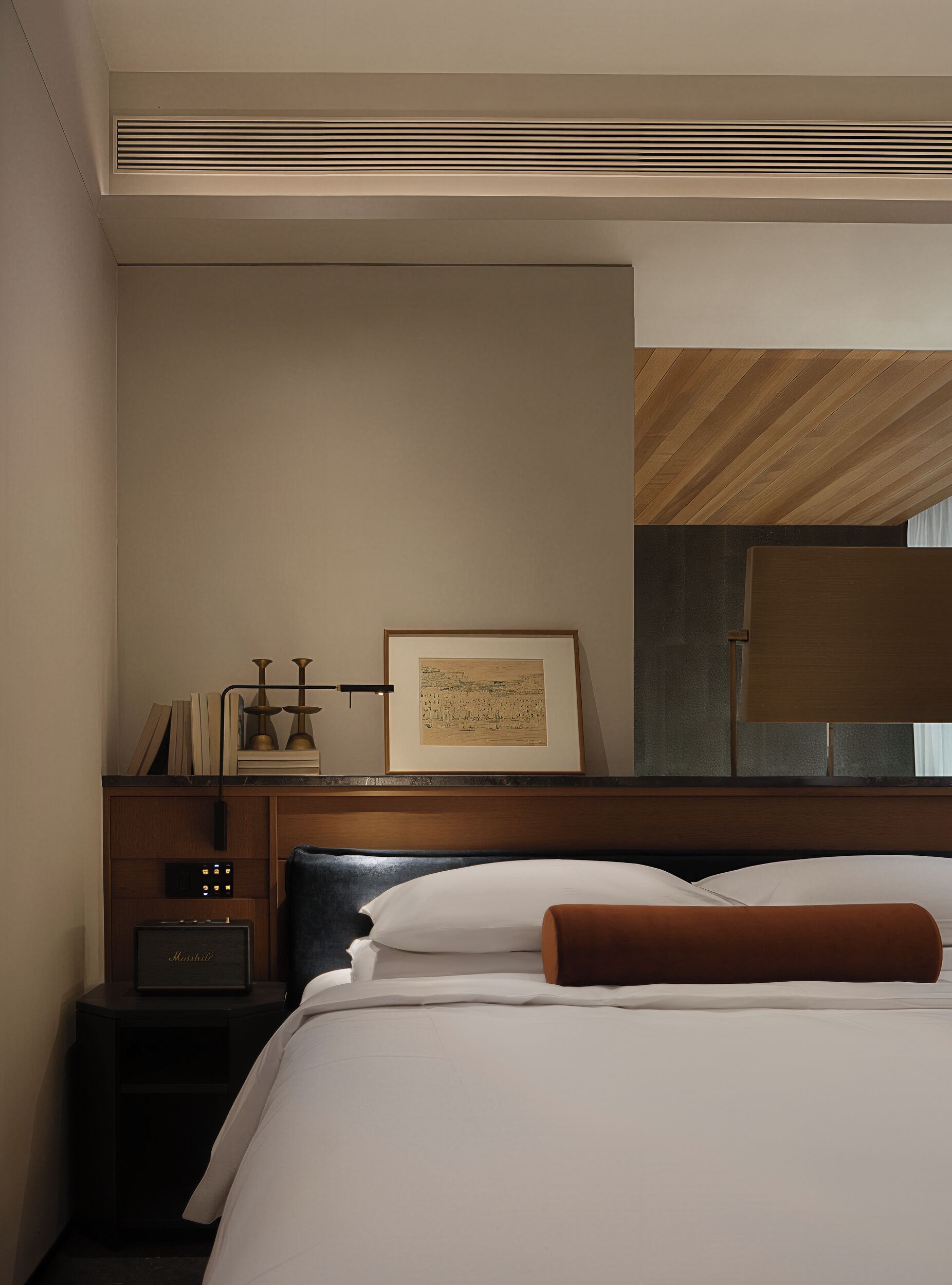 A hotel room with a bed, a nightstand with a lamp, a framed picture, and a wooden ceiling.
