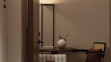 Una habitación moderna con una puerta de madera, un escritorio con lámpara, una silla y un florero con ramas.