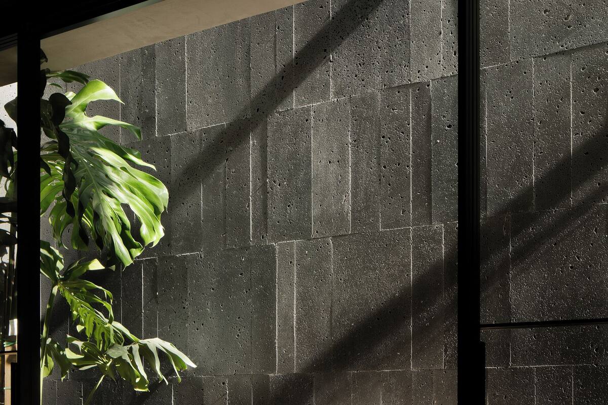 A modern outdoor seating area with a table and two wooden chairs, a potted plant, and a textured wall in the background.