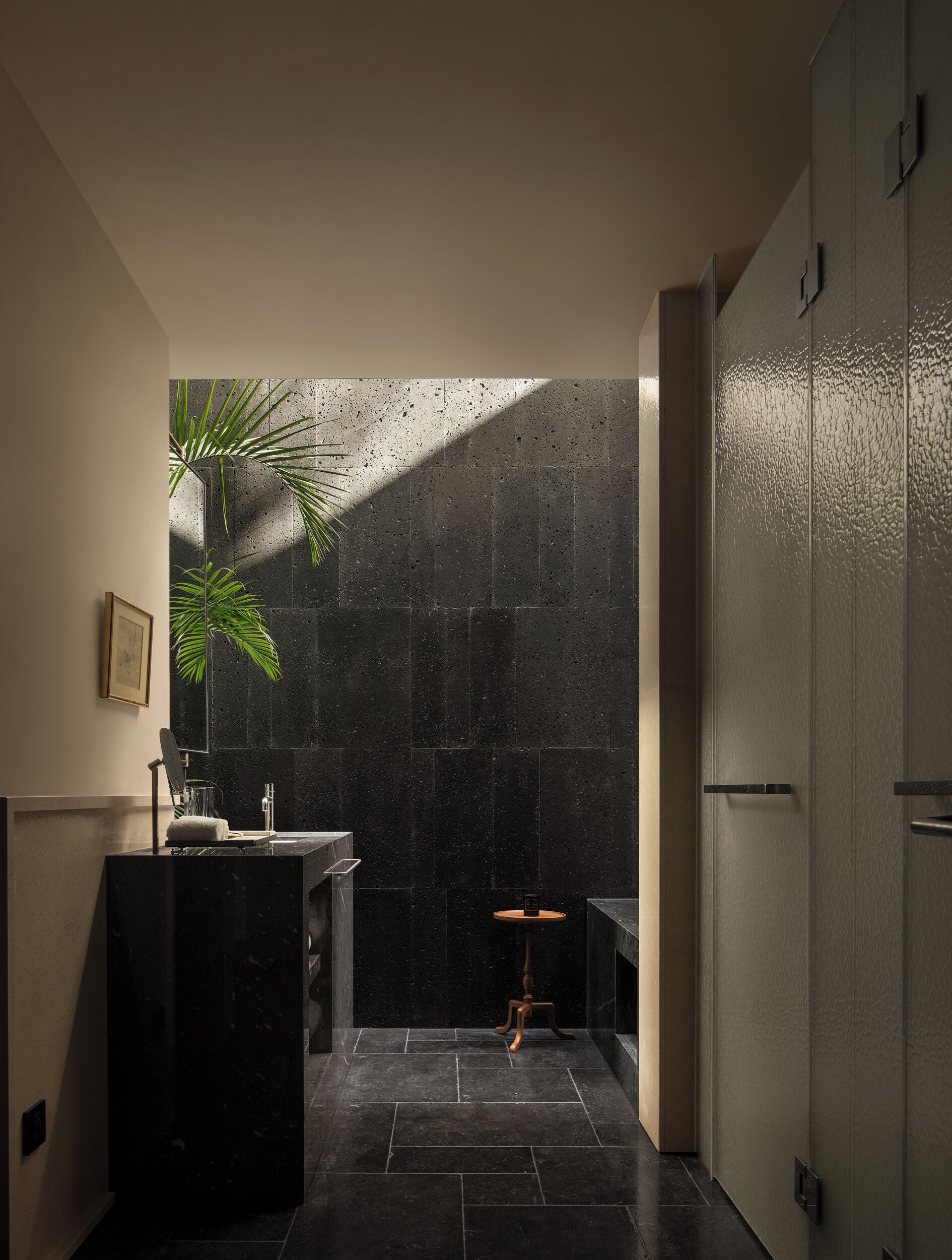 A modern bathroom with a large mirror, a sink, and a plant.