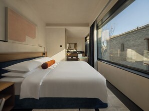 A modern hotel room with a large bed, a view of the city through a large window, and a small kitchenette in the background. - AnHeANAHATA (Datong)
