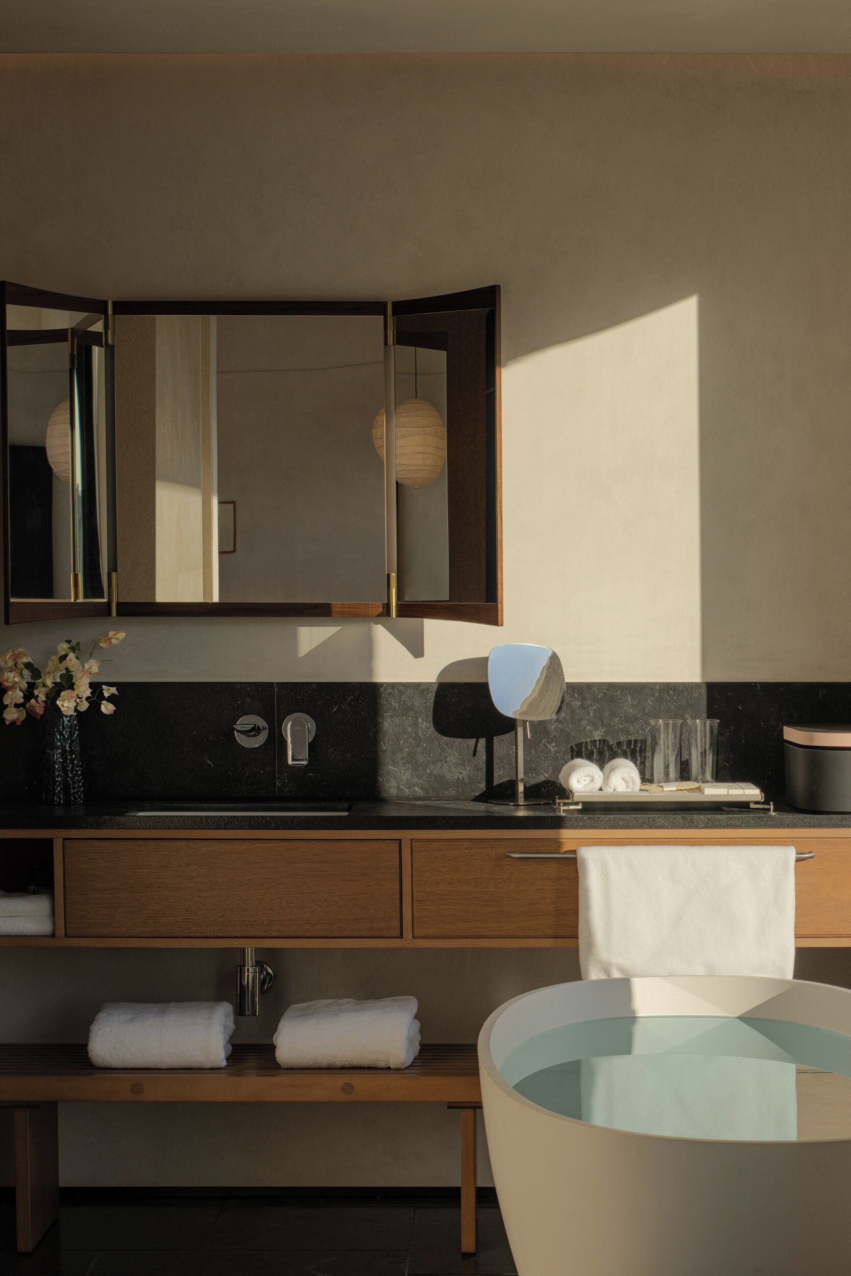 Un baño moderno con un espejo grande, un lavabo, un banco y una bañera redonda.