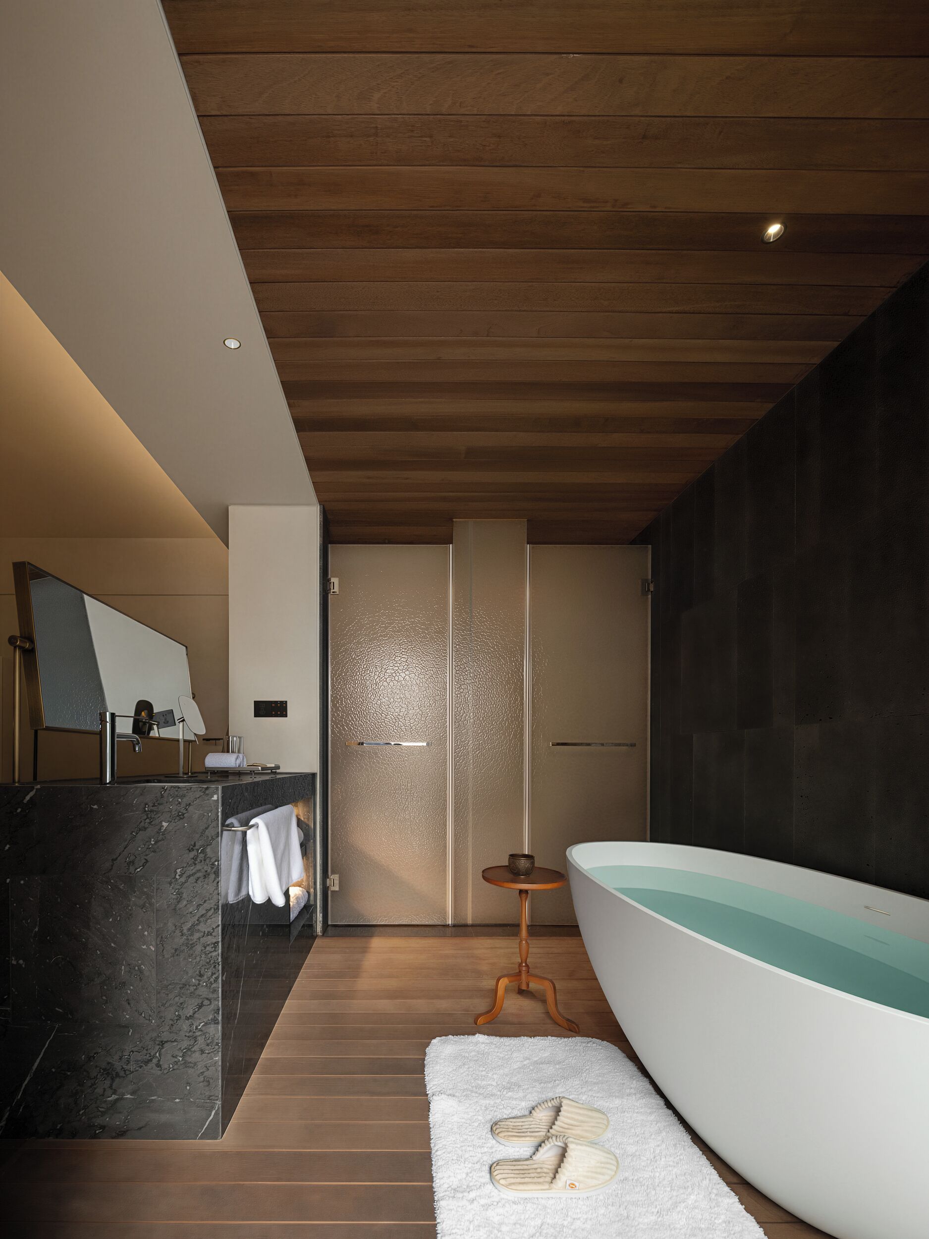 A modern bathroom with a freestanding bathtub, a vanity with a mirror, and a wooden floor.