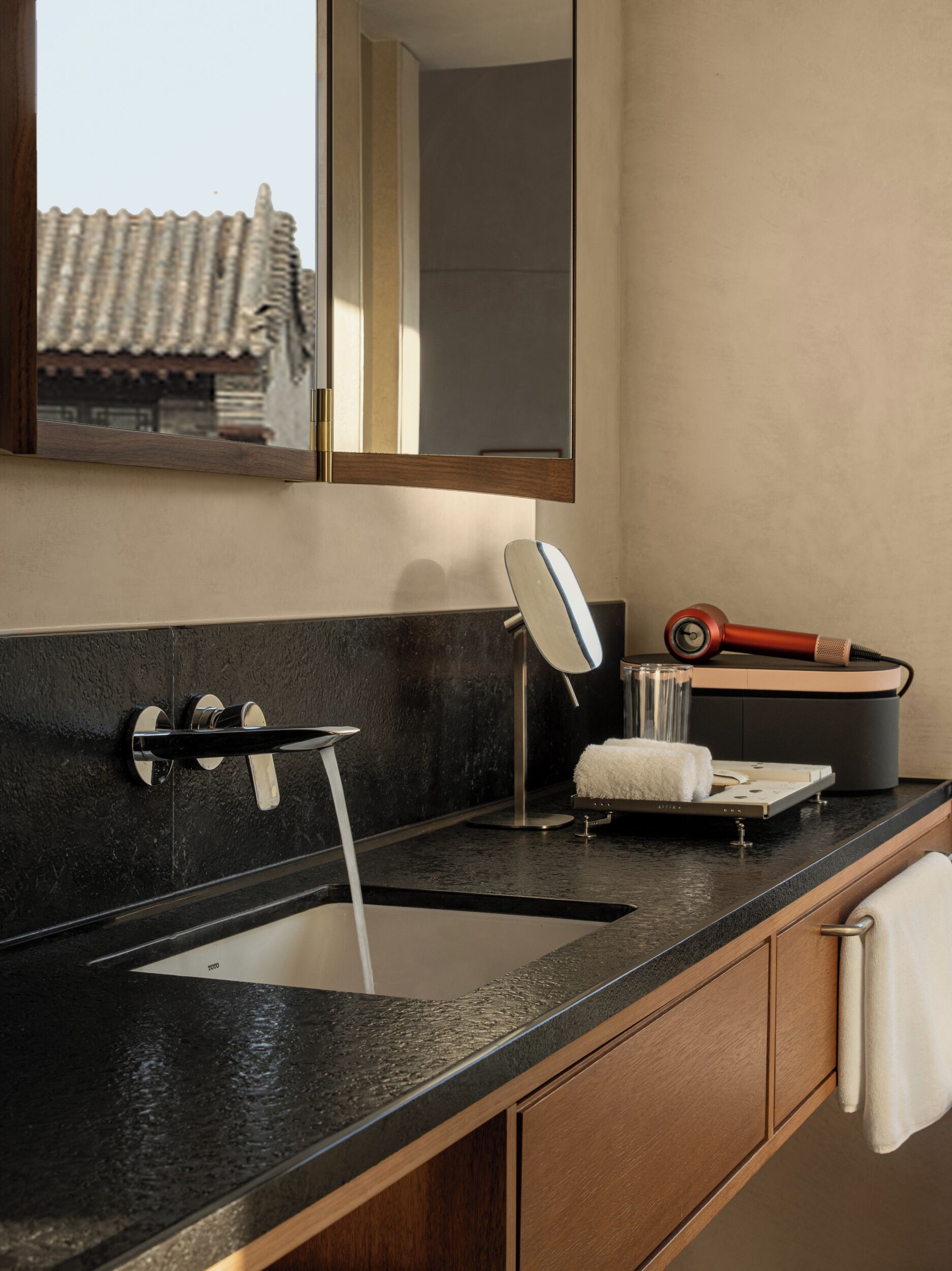 Un baño moderno con encimera negra, un lavabo con grifo, un espejo y un perchero para toallas.