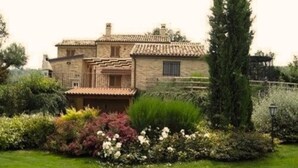 Una casa de piedra con techo de tejas, rodeada de un jardín cuidado con varios arbustos y césped.