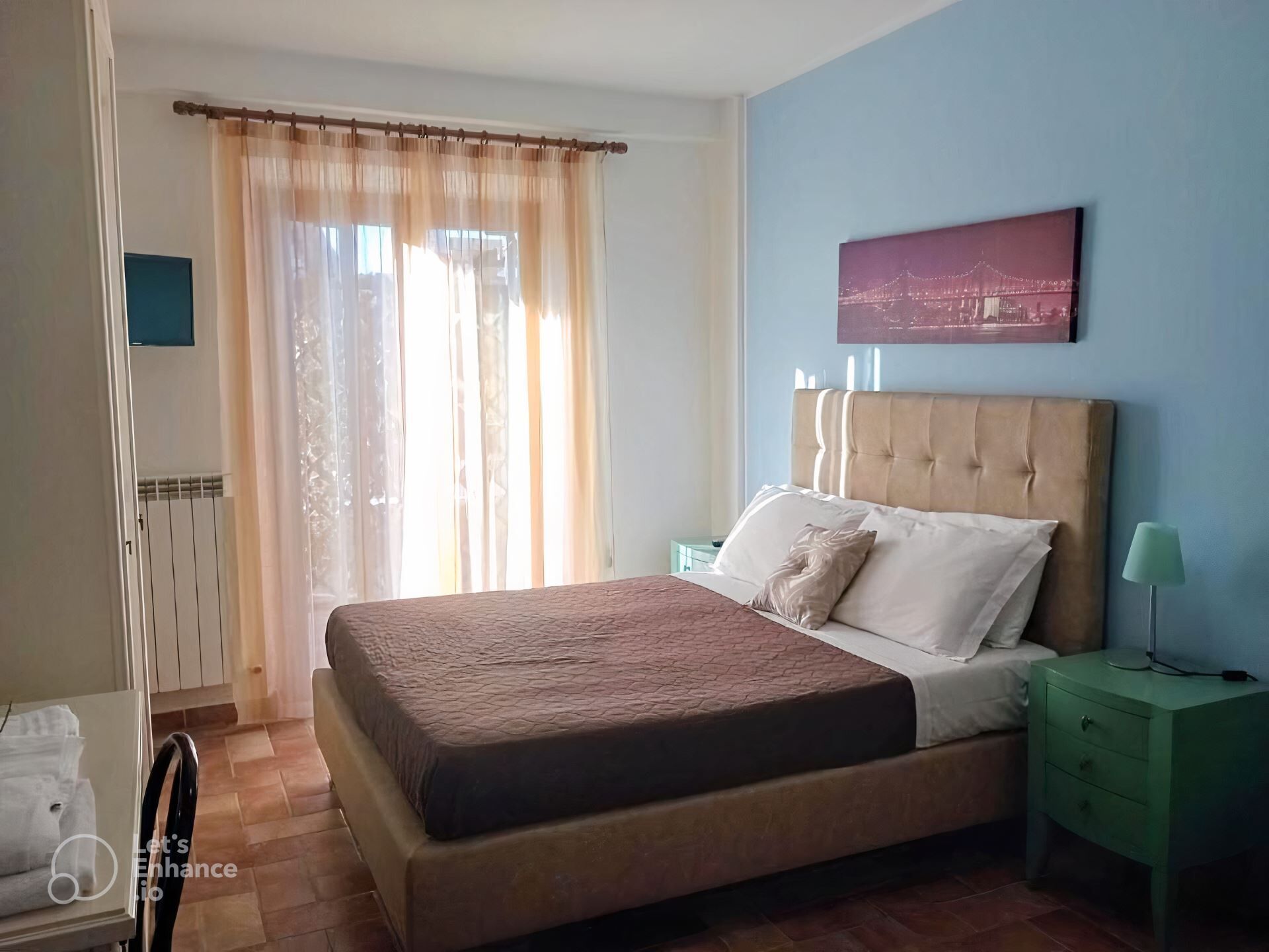 Un dormitorio con una cama, una mesita de noche, una lámpara, una ventana con cortinas y un cuadro en la pared.