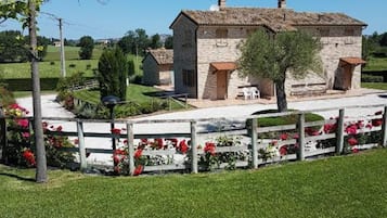 Una casa de piedra con techo de tejas, rodeada por una valla blanca y flores rojas.