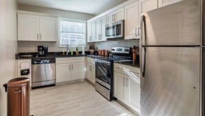 A modern kitchen with stainless steel appliances, white cabinetry, and a window providing natural light. - Olive Midtown Retreat Walkable, Stylish & Central (Memphis)