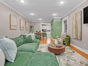Un salon avec un canapé vert, une table basse et un coin repas, avec une cuisine en arrière-plan.