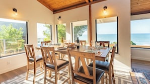 A dining area with a table set for four, wooden chairs, and large windows offering a view of the sea. - Pacific Seascape - An ocean front gem on the Mendocino coast! (Albion)