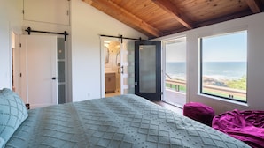 A bedroom with a large bed, a walk-in closet, a bathroom with a glass shower, and a view of the ocean. - Pacific Seascape - An ocean front gem on the Mendocino coast! (Albion)