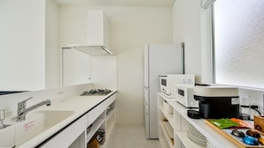 Una cocina compacta con armarios blancos, estufa a gas, microondas, refrigerador y ventana.