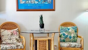 Ett rum med två fåtöljer i rotting, ett bord med glasskiva och ett flätat mönster i mitten, samt en inramad tavla på väggen.