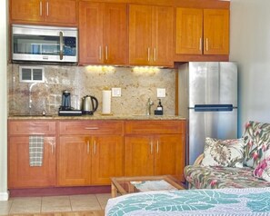 A compact kitchen with wooden cabinets, a stainless steel refrigerator, a microwave, and a coffee maker. - City-View Island Studio - WiFi - Parking (Honolulu)