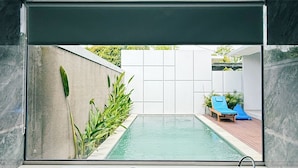 Ein modernes Badezimmer mit einer großen Badewanne und Blick auf Pool sowie Sitzgelegenheiten im Freien.
