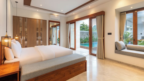 Ein modernes Schlafzimmer mit einem großen Bett, einer Bank und Blick auf einen Pool.