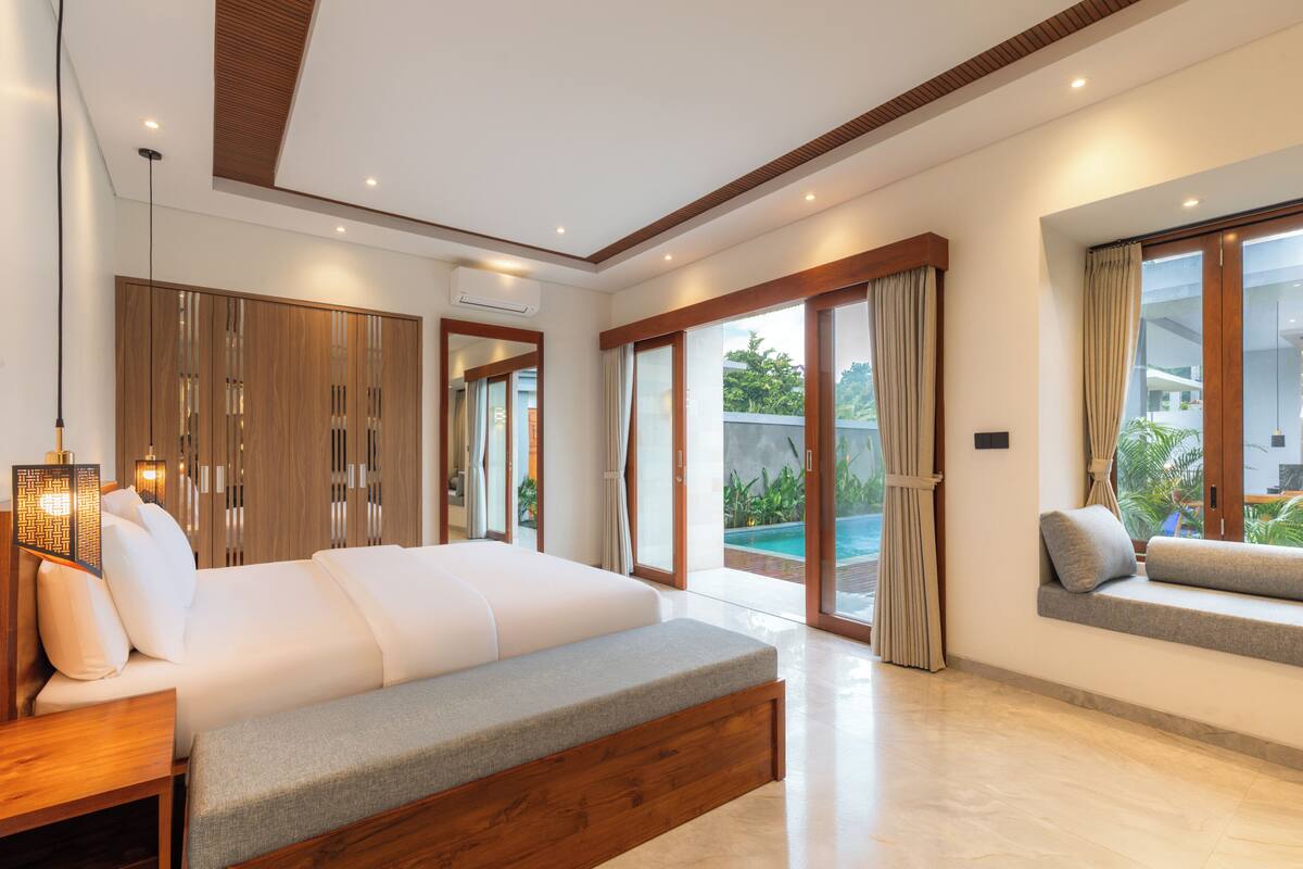 A modern bedroom with a large bed, a bench, and a view of a swimming pool.