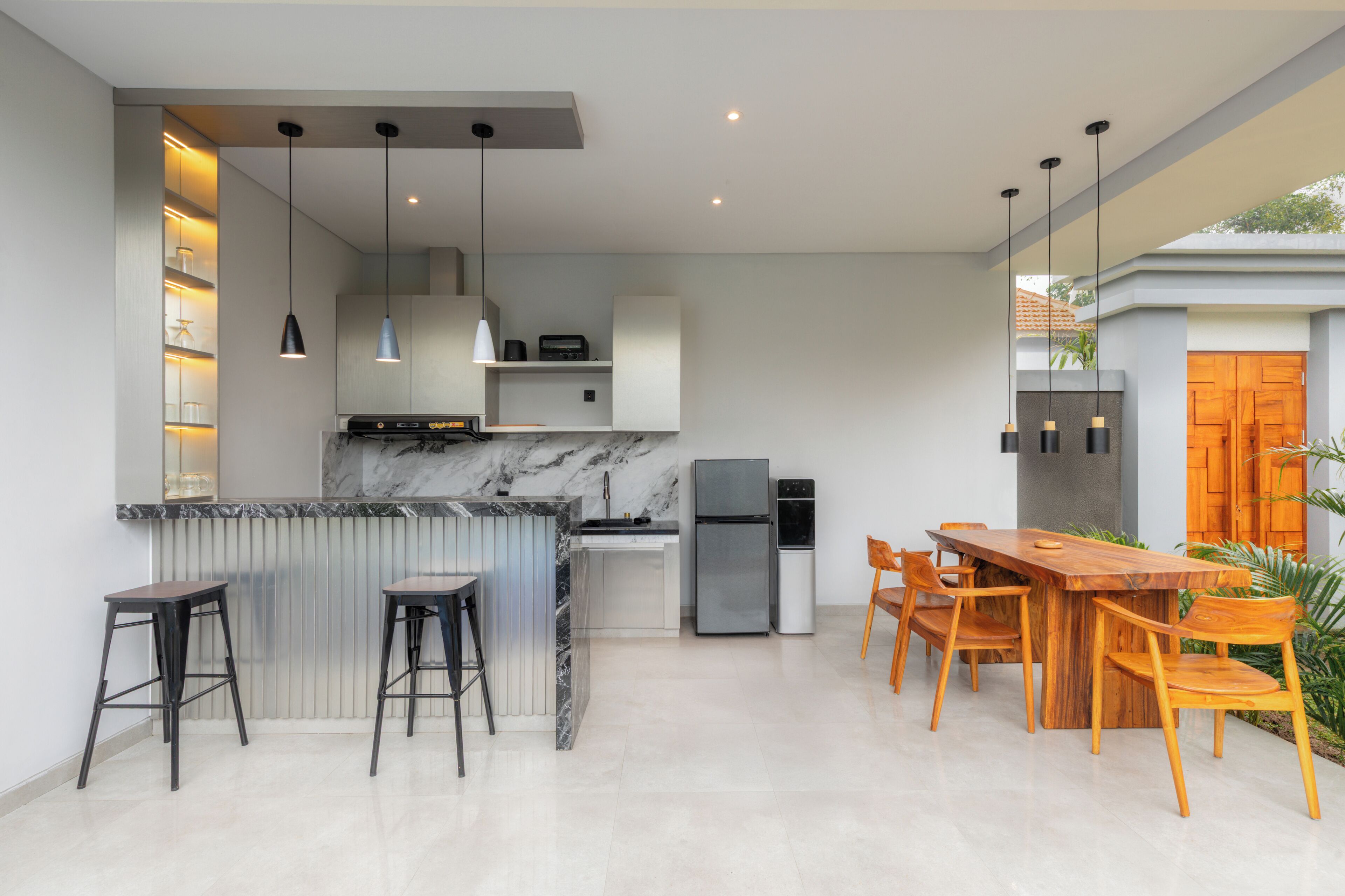 Una cocina moderna con una isla de mármol, taburetes de bar, una mesa de comedor de madera con sillas y electrodomésticos integrados.