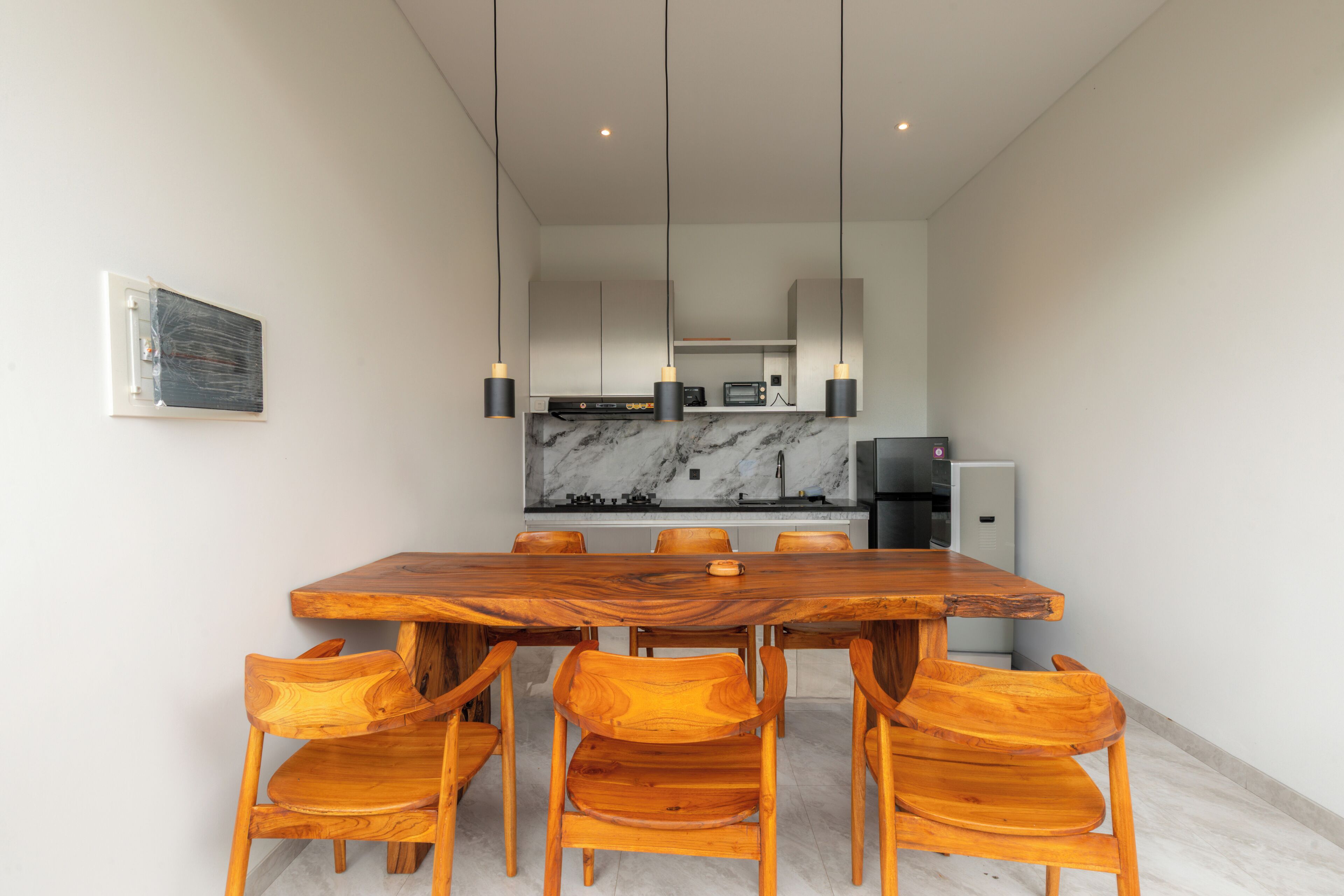 Un espace repas moderne avec une table et des chaises en bois, une cuisine en arrière-plan et des luminaires suspendus.