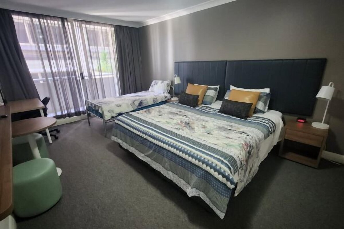 A hotel room with two single beds, a desk, a chair, and a small table.