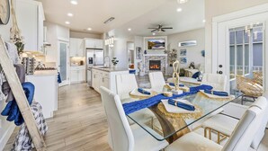 Une cuisine moderne avec des meubles blancs, un îlot central et un coin repas comprenant une table en verre et des chaises blanches.
