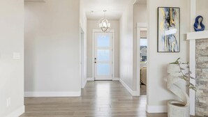 Un couloir doté d’un plancher en bois, une porte blanche au fond et un tableau abstrait moderne accroché au mur.