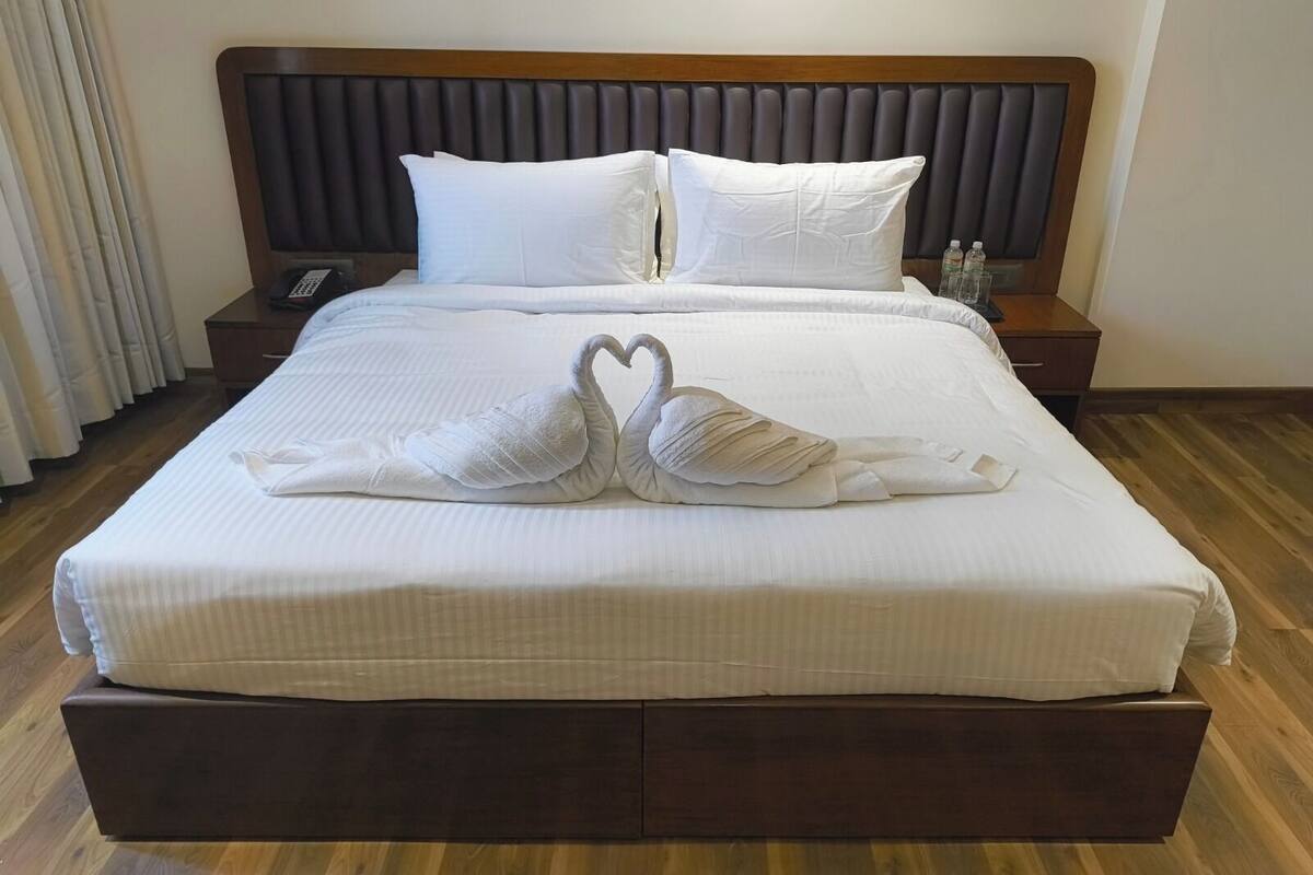 A neatly made bed with white linens and two swan-shaped towels on the bed.