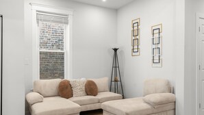 Ein modernes Wohnzimmer mit einem beige-farbenen Ecksofa, einem passenden Hocker und einer Stehlampe.
