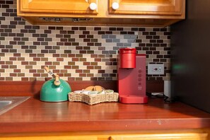Une cuisine avec un mur recouvert de carreaux, une bouilloire verte, une machine à café rouge et un panier de pain.