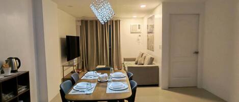 A dining area with a table set for six, a chandelier, and a sofa in the background.