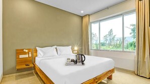 Moderni hotellihuone, jossa on puinen sänky, yöpöytä ja suuri ikkuna, jossa on verhot.