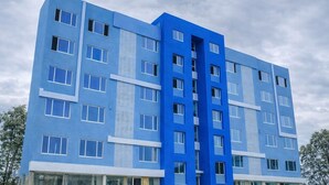 Monikerroksinen rakennus, jossa on sininen julkisivu, suuret ikkunat ja keskeinen, pystysuuntainen arkkitehtoninen elementti.