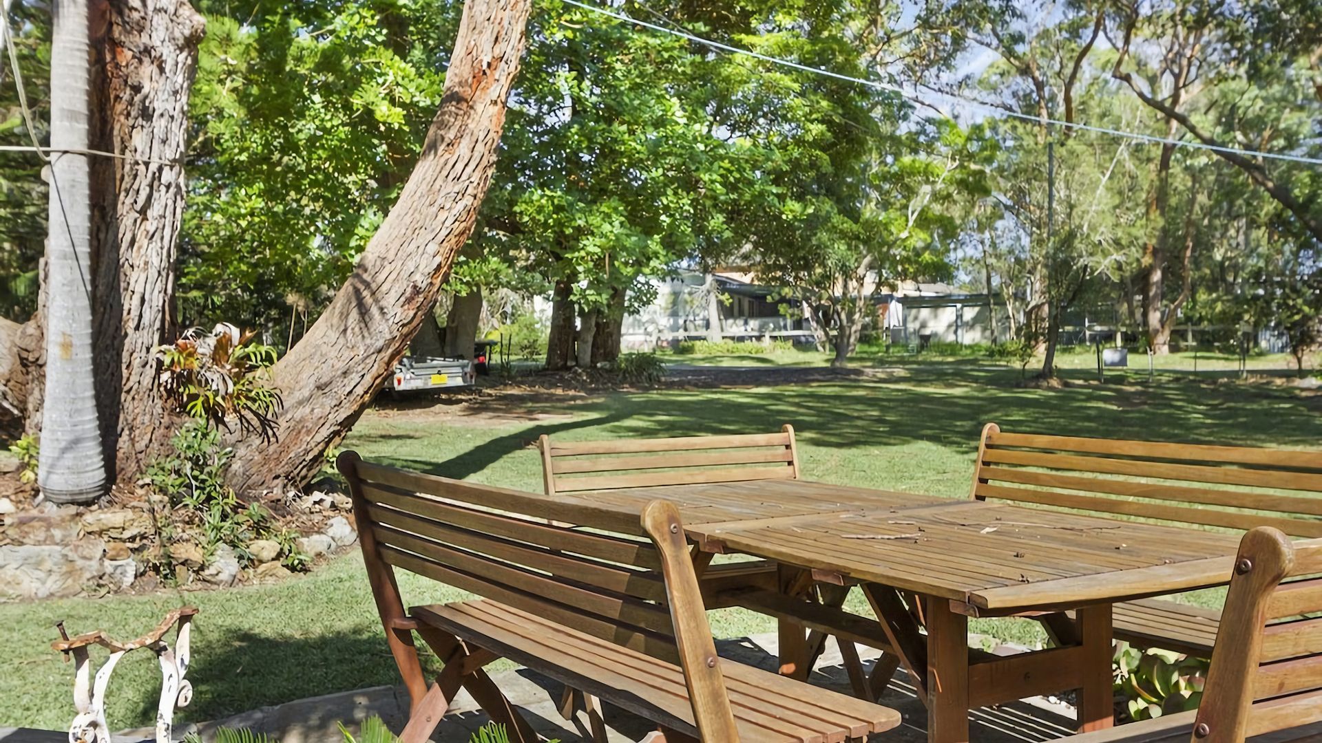 Een houten bankje en tafel staan in een park met bomen en een gazon.