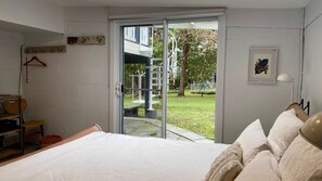 Ein Schlafzimmer mit Bett, Stuhl, Tisch und einer Glastür, die zu einem Außenbereich führt.