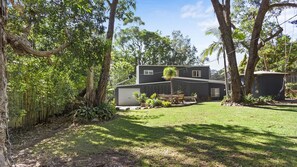 Une maison moderne à deux étages, dotée d’un patio couvert, et entourée d’une végétation luxuriante et d’arbres.